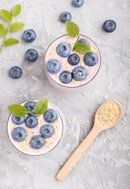 Joghurt mit Blaubeere und indischem Sesam in einem Glas- und Holzlöffel auf grauem konkretem Hintergrund