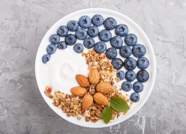 Joghurt mit Blaubeeren, Müsli und Mandeln in weißer Platte auf grauer Betonoberfläche. Draufsicht.