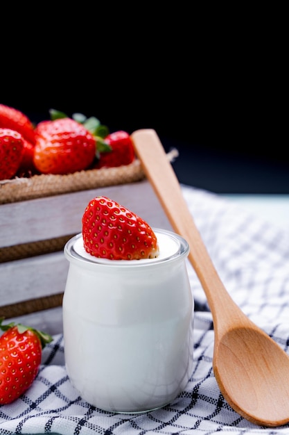 Joghurt mit Erdbeere und Holzlöffel und Erdbeeren in einer Holzkiste im Hintergrund