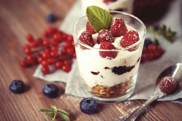 Joghurt mit frischen Beeren und Müsli serviert im Glasgefäß auf Holzhintergrund aus nächster Nähe