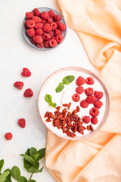 Joghurt mit Himbeer- und Goji-Beeren in Keramikschale auf Weiß