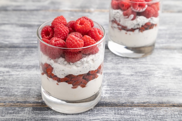 Joghurt mit Himbeere, Goji-Beeren und Chiasamen im Glas auf grauer Holzoberfläche