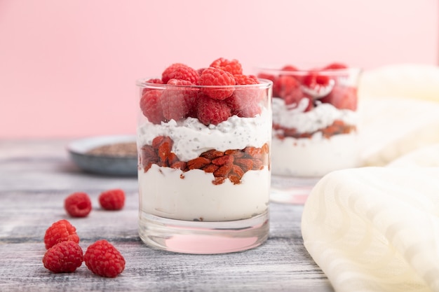 Joghurt mit Himbeere, Goji-Beeren und Chiasamen in Glas auf grauer Holzoberfläche und Leinentextil