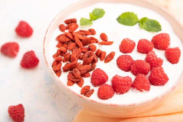 Joghurt mit Himbeere und Goji-Beeren in Keramikschale auf weißem Betonhintergrund Selektiver Fokus der Seitenansicht