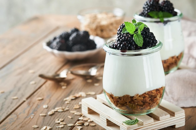 Joghurt mit Müsli, Brombeerbeeren und Müsli, serviert im Glasgefäß auf Holzhintergrund Gesundes Frühstückskonzept Gesundes Essen zum Frühstück von oben