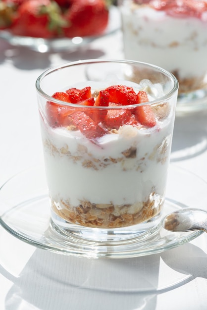 Joghurt mit Müsli und Erdbeeren im Glas auf einem weißen Tisch