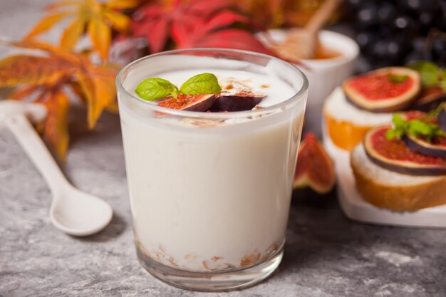 Joghurt mit Müsli und Feigenfrucht in einem Glas, Sandwich mit Frischkäse, Feigen und Honig serviert auf einem kleinen weißen Schneidebrett. Gesundes Essen . Herbsternte.