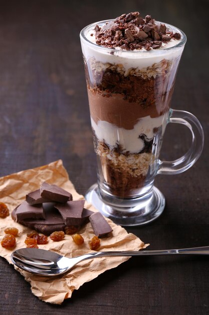 Joghurt mit Schokoladencreme, gehackter Schokolade und Müsli, serviert im Glas auf Holzhintergrund