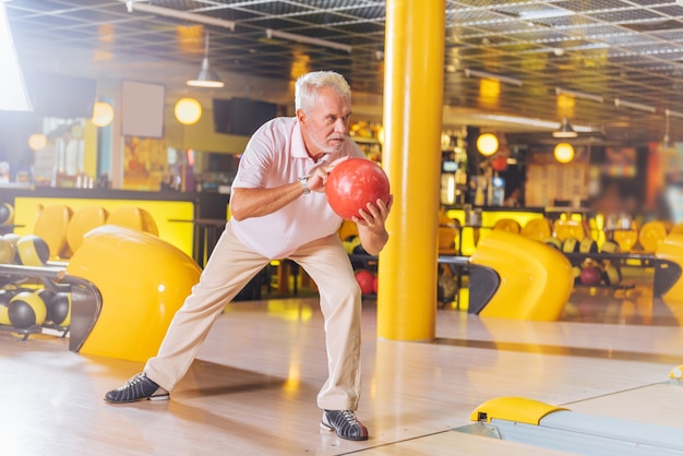 Jogo de boliche. bom homem idoso se preparando para lançar a bola enquanto joga boliche