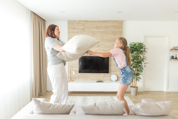 Jogos de família felizes mãe solteira e sua menina estão lutando almofadas e pulando no sofá
