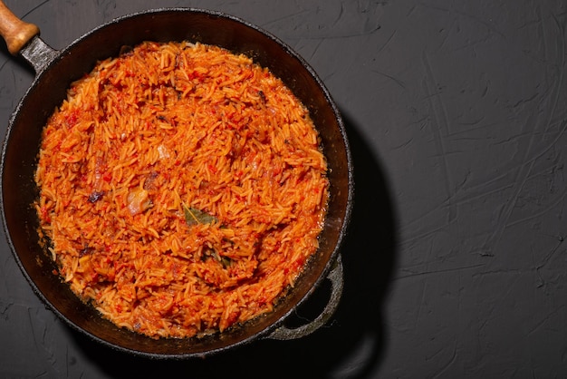 Jollof-Reis in einer Pfanne auf dunklem Hintergrund Ein traditionelles nigerianisches Gericht aus Reistomaten und Gewürzen