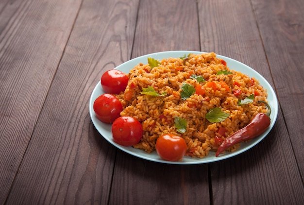 Jollof-Reis, Tomaten und Peperoni auf einer blauen Platte auf Holzhintergrund. Nationale Küche Afrikas.