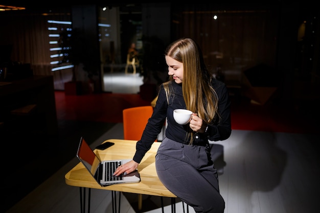 Jornada normal de trabajo de la mujer de negocios moderna. Hermosa joven sosteniendo una taza de café mientras está sentada en su lugar de trabajo