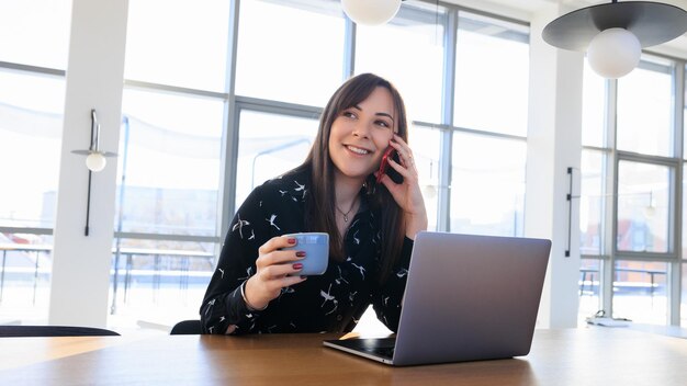 Jornada de trabajo independiente: una mujer joven hablando por teléfono y tomando café en un café