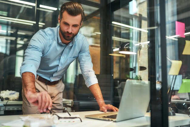 Jornada de trabajo joven y guapo empresario barbudo en ropa formal tomando anteojos mientras trabajaba en