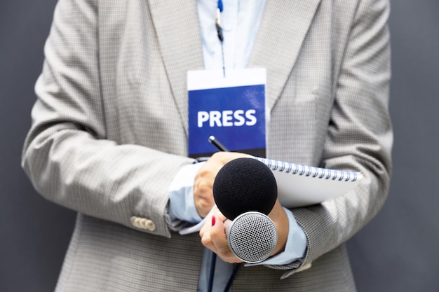 Foto jornalista em conferência de imprensa ou evento de mídia escrevendo notas segurando um microfone