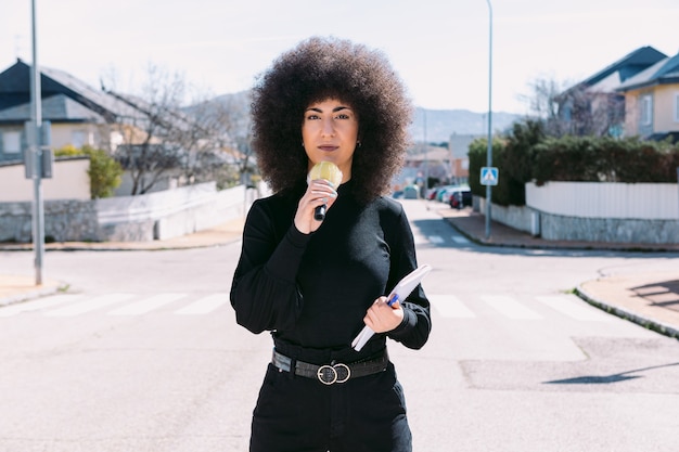 Jornalista repórter de televisão, com cabelo afro, em um noticiário na rua