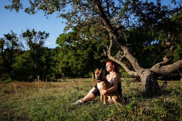 Jouful jovem acariciando seu cachorro vestindo roupas esportivas aproveitando seu tempo e férias no parque ensolarado