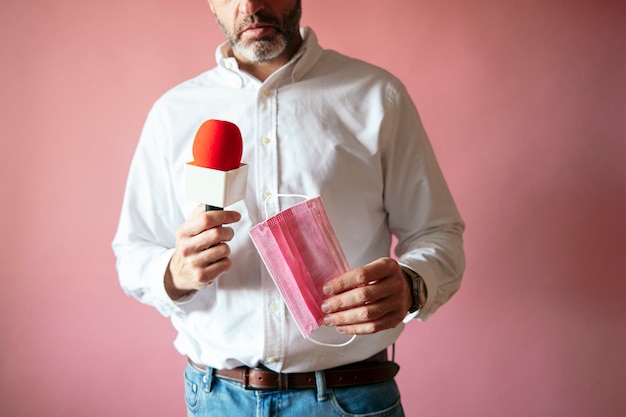 Journalist mit Maske und Mikrofon in der Hand auf rosa Wand