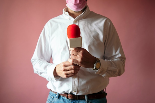 Journalist trägt Maske mit Mikrofon stehend mit rosa Hintergrund