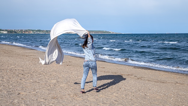 Jovem à beira-mar se diverte segurando um grande lençol ao vento, um estilo de vida livre.