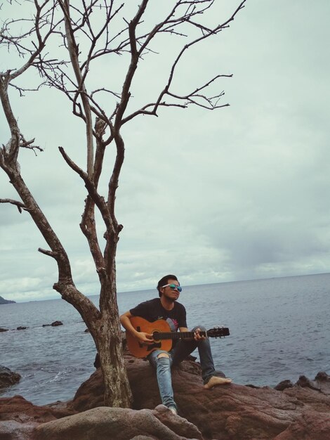 Foto jovem a tocar guitarra na praia contra o céu