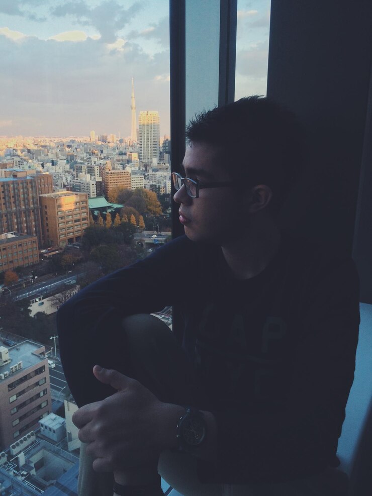Foto jovem a ver a cidade pela janela da casa