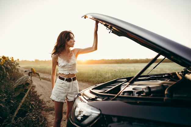 Foto jovem abrindo o capô de seu carro quebrado no campo