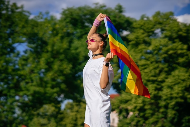 Jovem acenando a bandeira do orgulho LGBT no parque