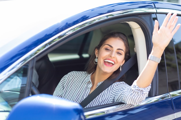 Jovem acenando. Mulher jovem e bonita dirigindo um carro acenando enquanto encontra um amigo na rua