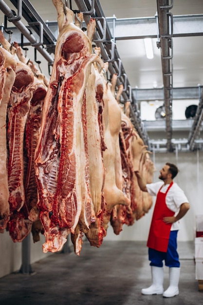 Foto jovem açougueiro na fábrica de carne ao lado da carne pendurada