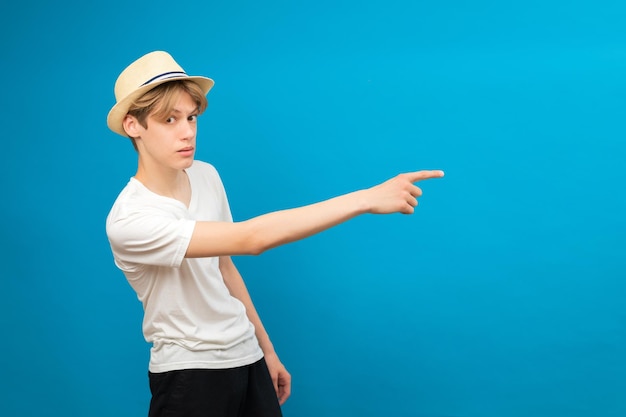 Jovem adolescente aponta as palmas das mãos de lado isoladas em azul Garoto bem-parecido e amigável prestando atenção no espaço da cópia melhor venda