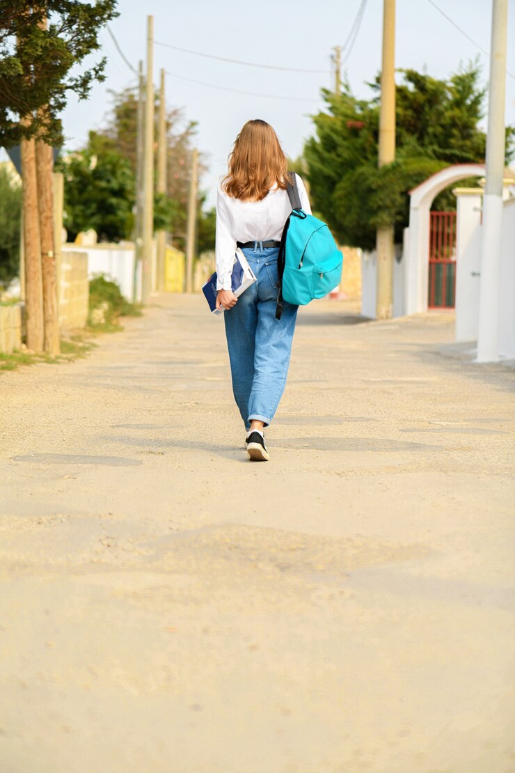 Foto jovem adolescente de jeans com mochila e livros vai a caminho da escola