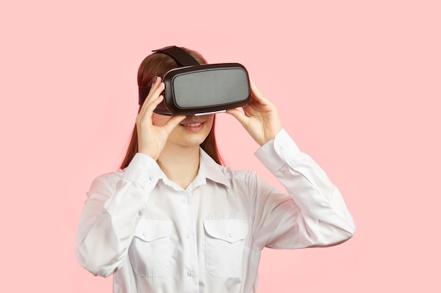 Jovem adolescente em um capacete de realidade virtual isolado em um fundo rosa joga um jogo de computador 3d.