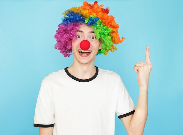 Foto jovem adolescente engraçado do sexo masculino com camiseta branca sobre fundo azul e peruca de palhaço com iedea