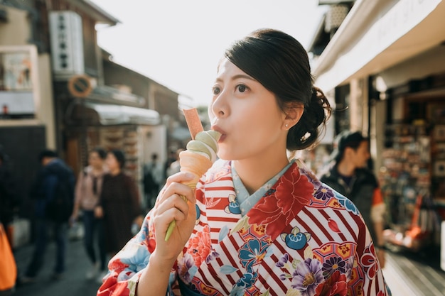 jovem adolescente japonesa em vestido de quimono de flores junta-se a divertir-se no festival de verão junta-se à feira do templo. mulher feliz em pano tradicional comendo sorvete matcha kyoto japão na rua fervilhante quente