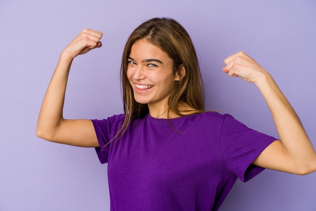 Foto jovem adolescente magrinha caucasiana em fundo roxo mostrando força gesto com os braços, símbolo do poder feminino