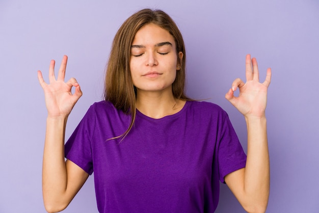 Jovem adolescente magrinha caucasiana em fundo roxo relaxa após um duro dia de trabalho, ela está realizando ioga.