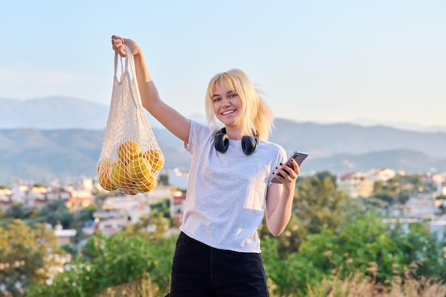 Jovem adolescente segurando um saco ecológico de malha com laranjas orgânicas frescas