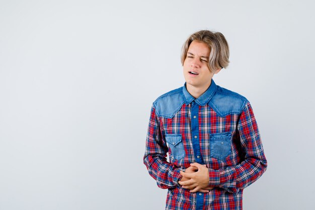 Jovem adolescente sofrendo de dor de estômago na camisa e parecendo incomodado. vista frontal.