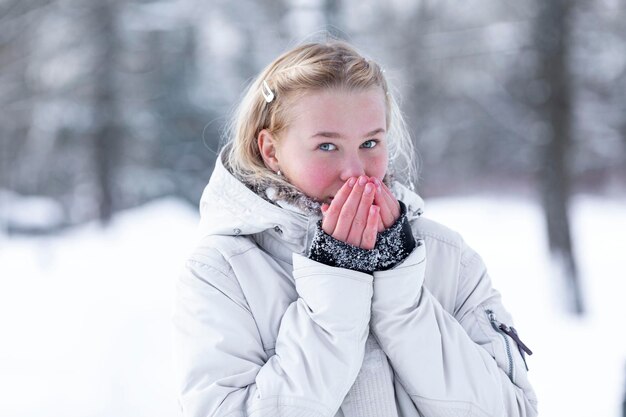Jovem adolescente sorridente em um parque nevado Loira bonita em uma jaqueta branca andando ao ar livre no inverno e nas estações frias Closeup