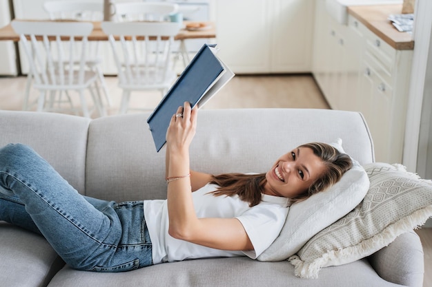 Jovem adulta caucasiana lê livro em casa deitada no sofá Mulher hispânica bonita gosta de literatura