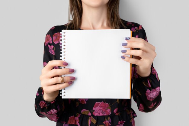 Jovem adulta com vestido segurando um bloco de notas em branco aberto