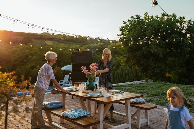 Jovem adulta e idosa organizando mesa de jantar juntos no quintal