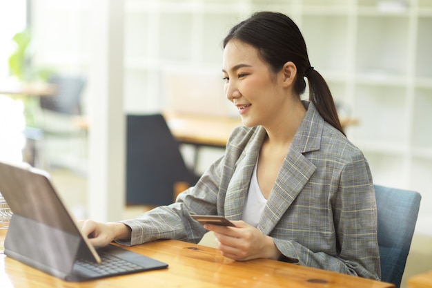 Jovem adulto asiático segurando um cartão de crédito e usando tablet digital para pagamento online