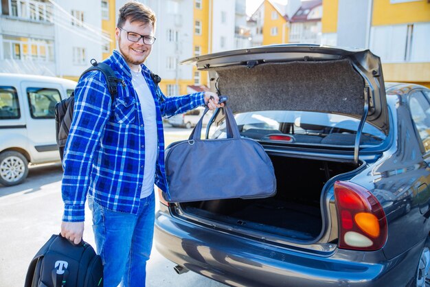 Foto jovem adulto colocando saco no porta-malas do carro conceito de viagem de carro