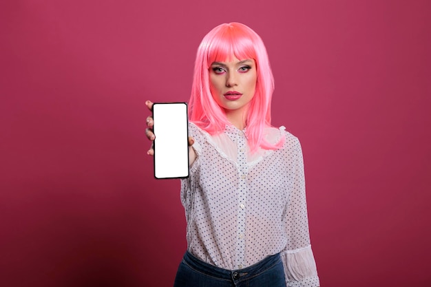 Jovem adulto com cabelo rosa mostrando smartphone com tela branca e exibição de chroma key isolado na frente da câmera. Segurando o modelo de maquete de copyspace em branco no aplicativo para celular.