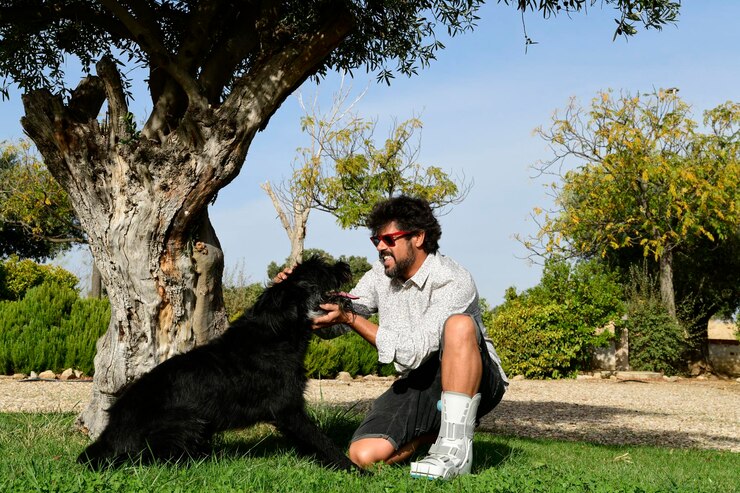 Foto jovem adulto com pé fraturado e bota andador brincando com seu animal de estimação, um cão schnauzer preto,