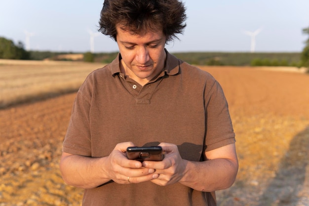 Jovem adulto enviando mensagens de texto ou consultando o smartphone no campo ou conceito de cobertura global do ambiente rural