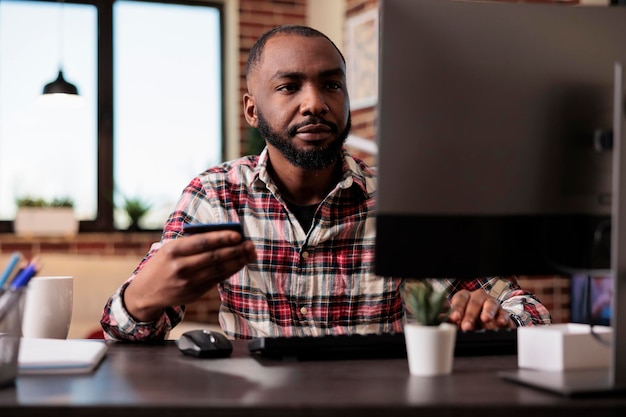 Jovem adulto fazendo compras on-line no computador, usando cartão de crédito para fazer transações de pagamento eletrônico. Comprando roupas no site da loja de varejo com compra com desconto, trabalhando remotamente em casa.